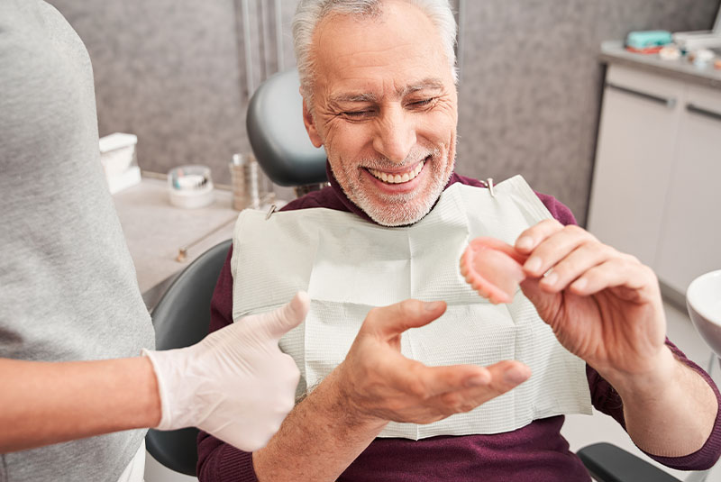 Dentist showing to senior patient teeth dentures