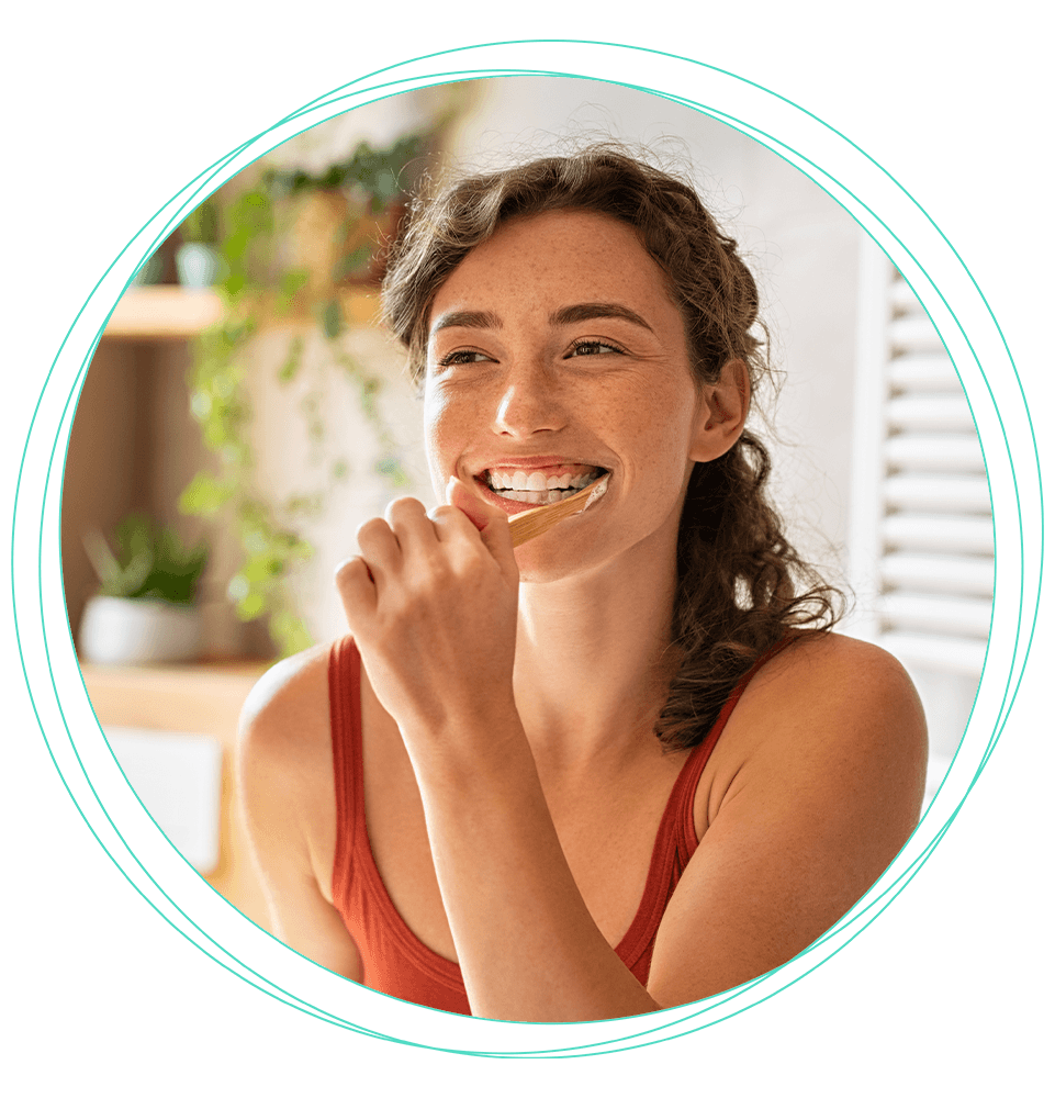 young female smiling while brushing their teeth in their bathroom